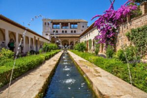 The tranquil Generalife gardens in the Alhambra, with water jets arching over a long pool and bright flowers blooming along the paths.