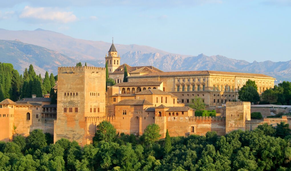 A panoramic view of the Alhambra palace complex in Granada, Spain, with the Sierra Nevada mountains in the background.