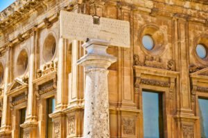 Close-up of a stone column and Latin inscription in front of the Renaissance façade of the Palace of Charles V at the Alhambra, Granada.
