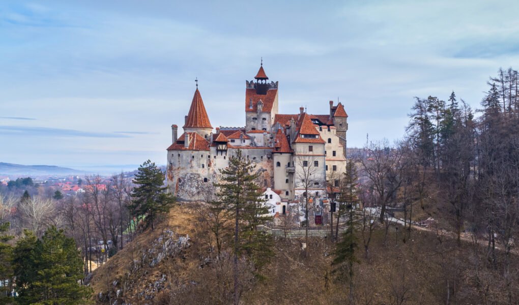 Bran Castle perched on a rocky hilltop in winter, surrounded by leafless trees and overlooking the village of Bran in Transylvania, Romania