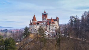Bran Castle perched on a hilltop in Transylvania, surrounded by trees and distant mountains.