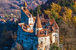 Aerial autumn view of Bran Castle in Transylvania, surrounded by trees and historic buildings.