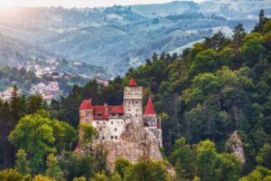 Bran Castle surrounded by lush Transylvanian forests and mountain landscape at sunset
