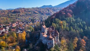 Aerial photo of Bran Castle surrounded by colorful autumn forest in Transylvania.