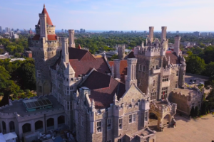 Drone view of Casa Loma’s detailed Gothic Revival architecture with red-tiled rooftops and chimneys, surrounded by greenery in Toronto, Canada.