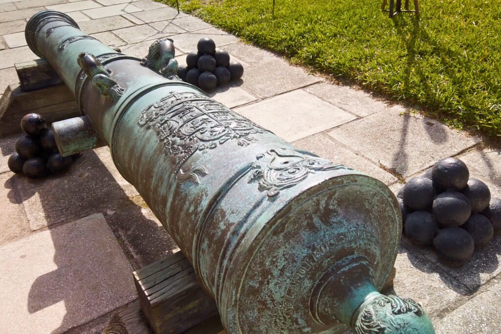 Primer plano de un cañón de bronce ornamentado con el escudo real español y bolas de cañón apiladas en el Castillo de San Marcos, en St. Augustine, Florida.