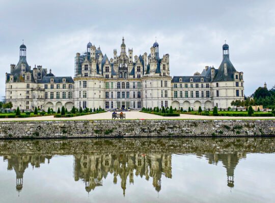Front view of Château de Chambord in France reflected in a still moat under a cloudy sky, showcasing its grand Renaissance architecture.