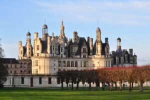 Château de Chambord bathed in soft winter light, its ornate towers rising above manicured lawns and rows of bare trees.