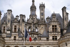 Close-up of the ornate rooftop and towers of Château de Chambord, with the French flag waving in the foreground.
