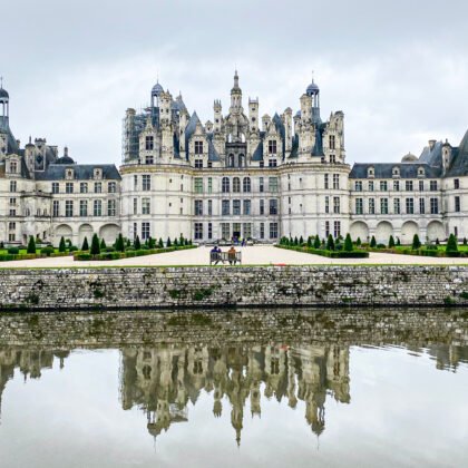 Château de Chambord in the Loire Valley, France, showcasing its stunning French Renaissance architecture with intricate towers and turrets reflected in the water on a cloudy day.