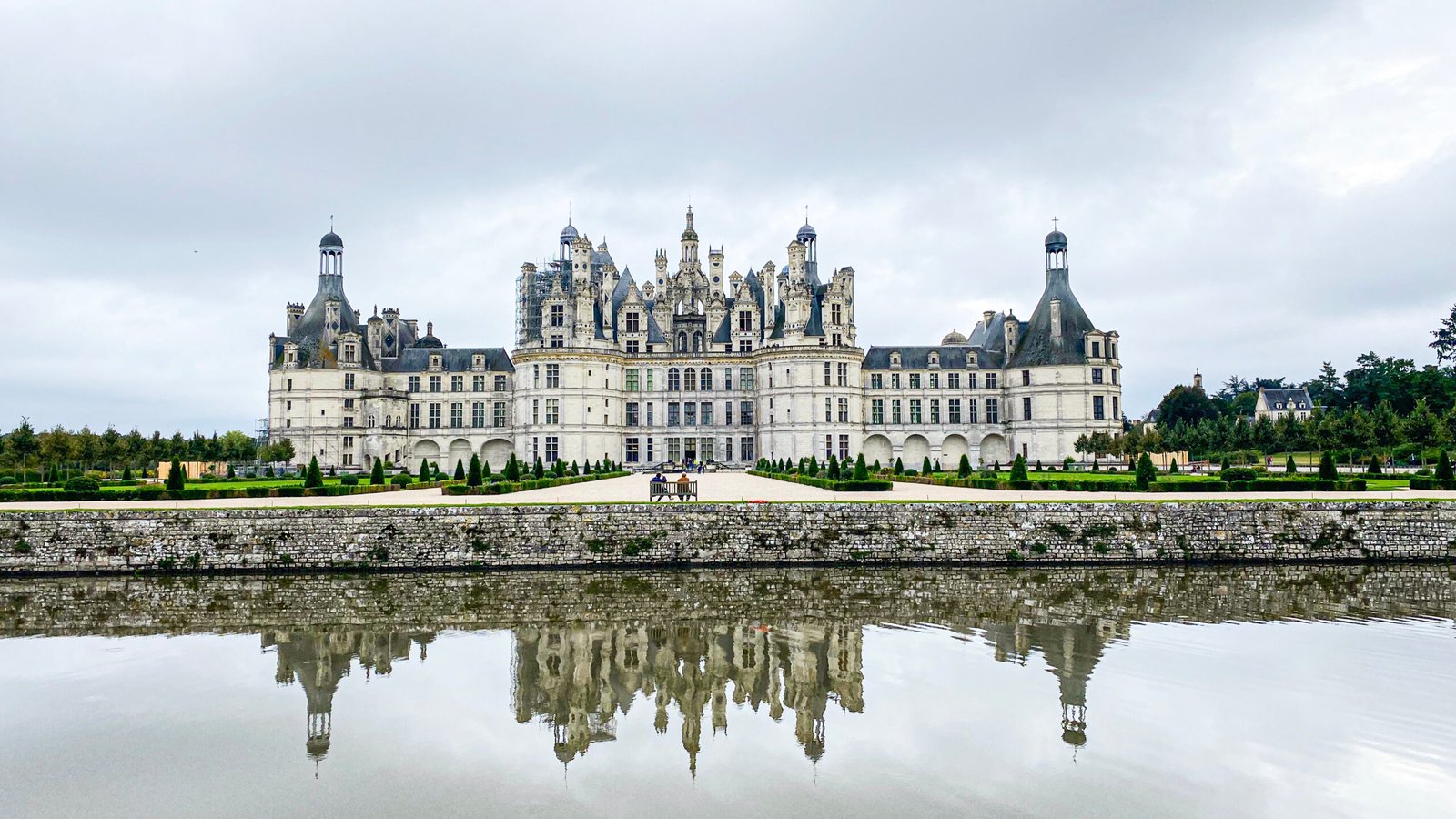 Front view of Château de Chambord in France reflected in a still moat under a cloudy sky, showcasing its grand Renaissance architecture.