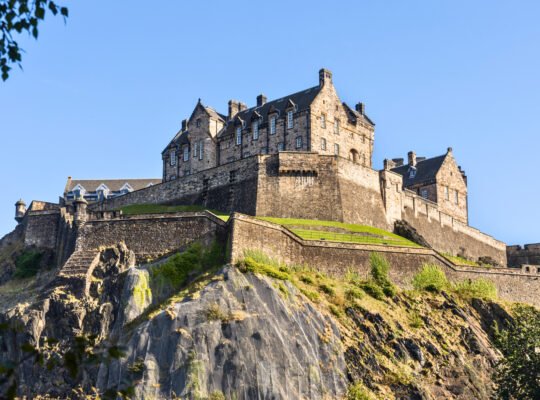 Edinburgh Castle perched atop the rugged cliffs of Castle Rock under a clear blue sky.