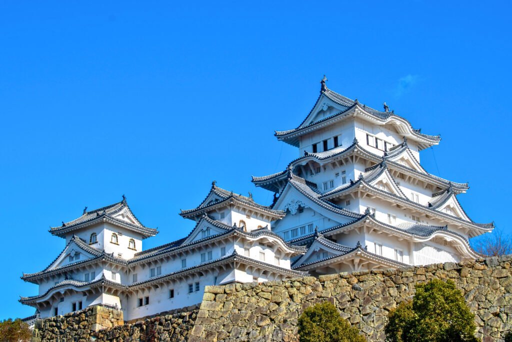 Bright daytime view of Himeji Castle’s elegant white structure with traditional curved rooftops, standing tall against a vibrant blue sky.