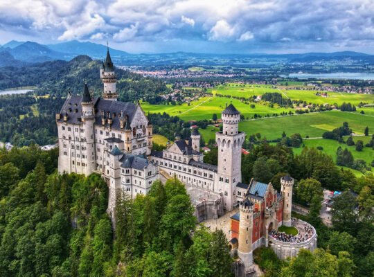 Aerial view of Neuschwanstein Castle surrounded by green valleys and mountains in Bavaria, Germany
