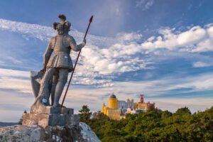 Statue overlooking vivid Pena palace with dramatic sky and pine trees in Sintra, Portugal