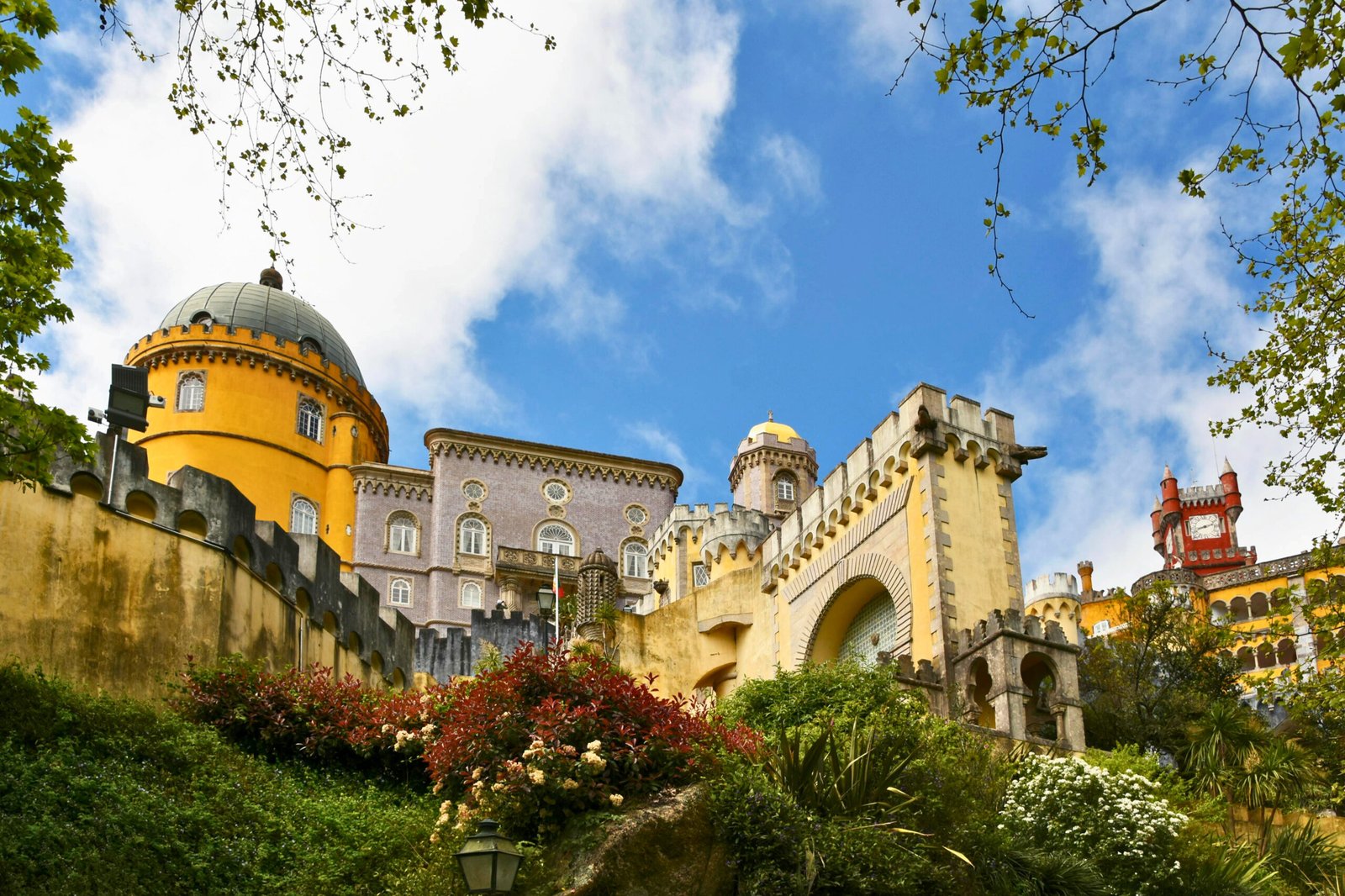 A lush garden leads to the whimsical architecture of Pena Palace beneath a spring sky in Sintra.