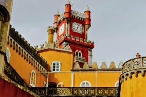 The bright clock tower of Pena Palace in Sintra, Portugal, with vivid red and yellow walls under daylight.