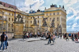 Crowds gathered at the ornate entrance of Prague Castle under bright skies