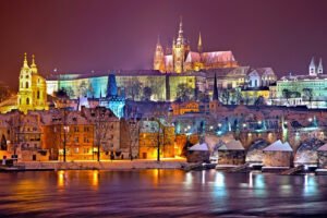 Prague Castle at night with lights reflecting on the river.
