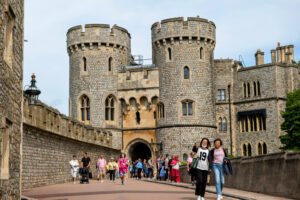 Visitors walking along the approach to Windsor Castle with stone towers and medieval walls in the background.