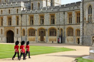 Guards in red uniforms and bearskin hats marching in front of Windsor Castle’s stone walls during the Changing of the Guard ceremony.
