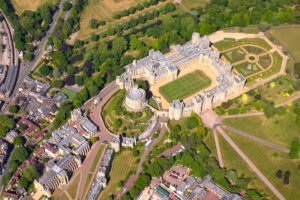 Aerial view of Windsor Castle, showing its sprawling grounds, gardens, and circular Round Tower at the center.