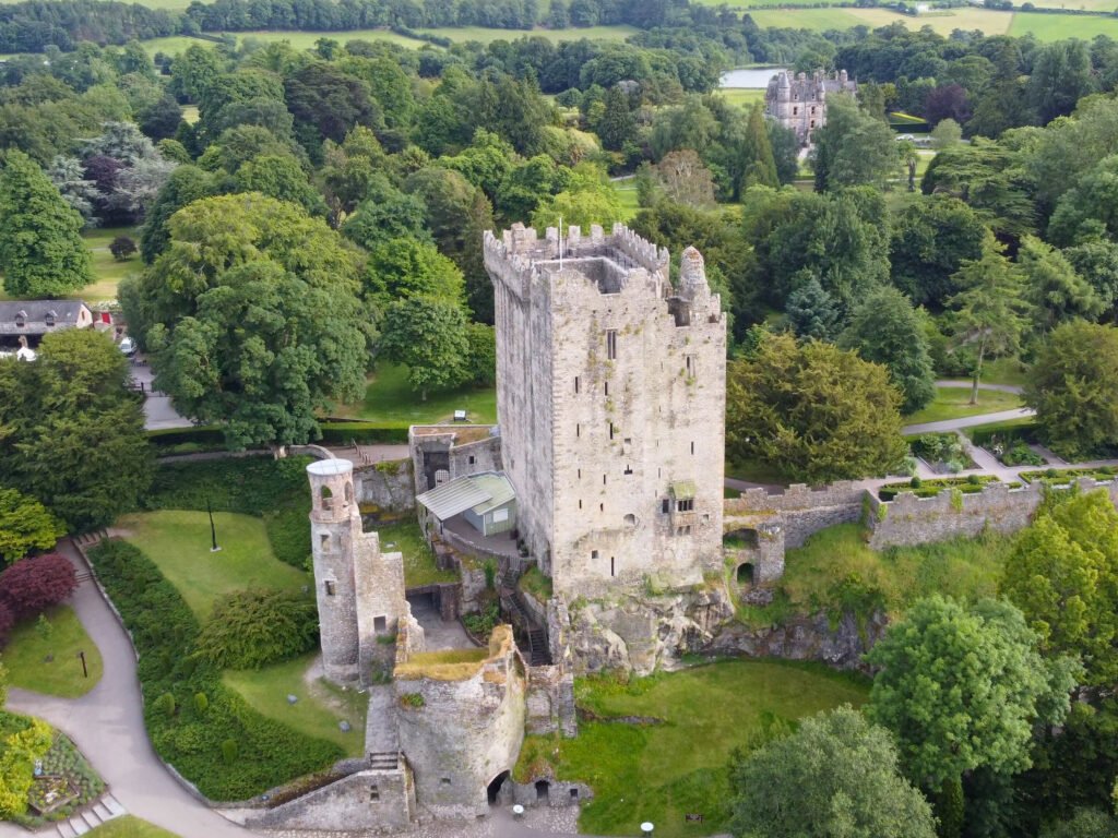 Aerial view of Blarney Castle in Ireland, featuring its medieval stone tower surrounded by lush gardens and greenery.