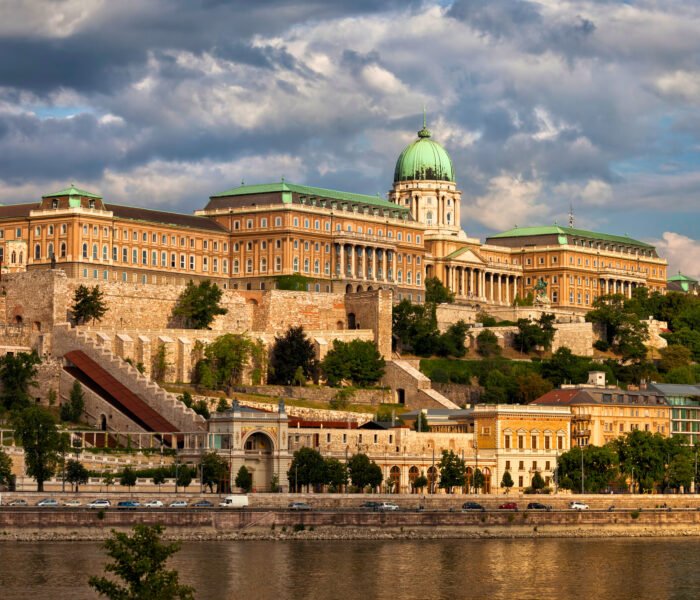 Panoramic view of Buda Castle overlooking the Danube River in Budapest, Hungary, with dramatic skies highlighting the historic Baroque palace.
