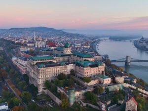 Aerial view of Buda Castle in Budapest at sunrise with the Danube River and historic cityscape.