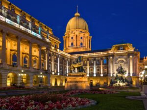 Budapest Castle glowing at night with gardens and statues in the foreground, focus on Budapest Castle.