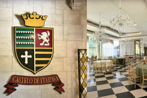 Interior view of the Castelo de Itaipava banquet hall with crystal chandeliers, checkered floors, and the castle’s official crest displayed on a stone wall.