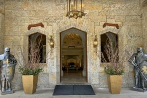 Medieval-style entrance of Castelo de Itaipava featuring stone walls, armored knight statues, chandeliers, and decorative lanterns welcoming guests inside.