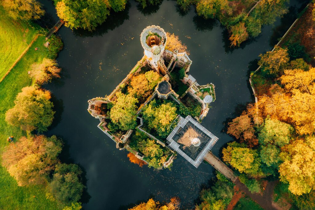 Top-down autumn view of la Mothe-Chandeniers surrounded by a forest of golden trees and a dark reflective moat, showing trees growing within the castle ruins.