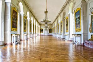 The Gallery of Great Battles at the Palace of Versailles, featuring a long parquet floor, arched windows, crystal chandeliers, and gilded frames showcasing historical paintings.