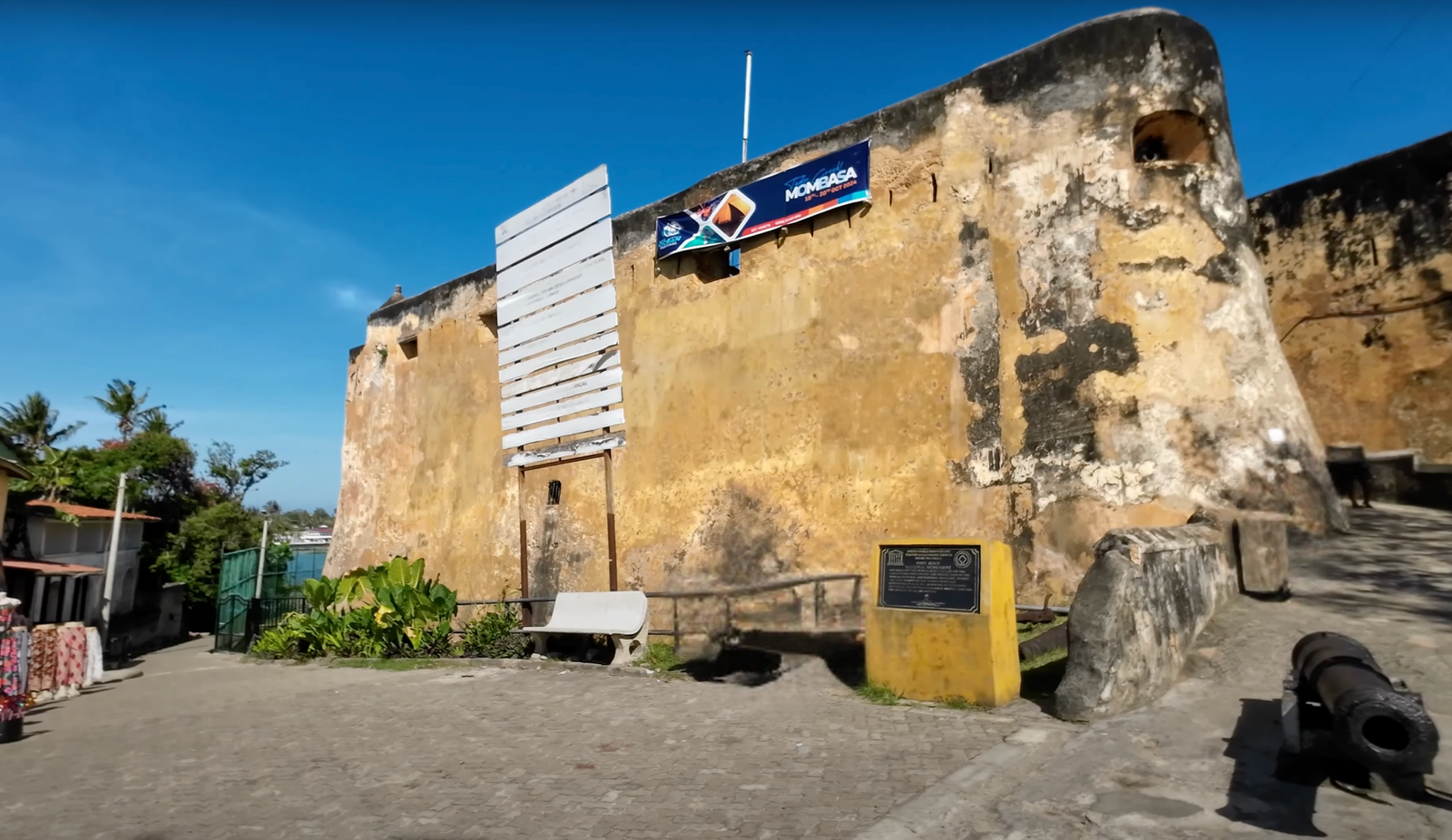 Entrance to Fort Jesus in Mombasa, featuring weathered coral stone walls, a UNESCO World Heritage Site plaque, and a cannon beside a paved path.