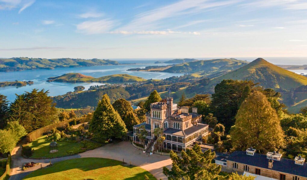Aerial view of Larnach Castle surrounded by lush gardens and overlooking the Otago Peninsula and harbor in Dunedin, New Zealand.