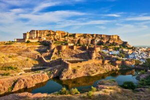 Wide-angle view of Mehrangarh Fort overlooking Jodhpur’s blue city and surrounding lakes, with golden sunlight illuminating the fortress walls.