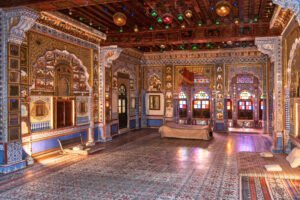 Lavishly decorated interior of Phool Mahal in Mehrangarh Fort, Jodhpur, showcasing intricate wall art, stained glass windows, and royal seating.