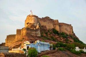 View of Mehrangarh Fort rising above the rocky hill of Jodhpur, with colorful local houses and temples nestled at its base.