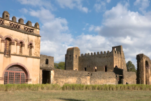 View of various historic buildings inside the Fasil Ghebbi complex in Gondar, Ethiopia, including arched windows, stone towers, and partially ruined walls.