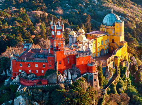 Aerial view of Pena Palace in Sintra, surrounded by lush forest and vibrant colors.