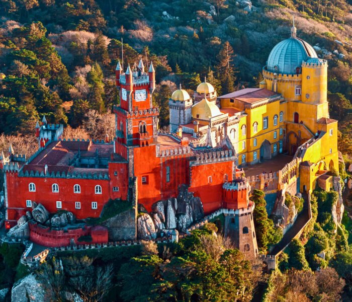 Aerial view of colorful Pena Palace in Sintra, Portugal, surrounded by forested hills.