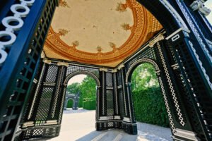 Interior view of a decorative garden pavilion at Schönbrunn Palace with arched lattice walls, floral ceiling paintings, and views of lush greenery outside.