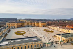 Aerial view of the grand forecourt of Schönbrunn Palace, with symmetrical layout, fountains, and distant hills framing the Gloriette in the background.