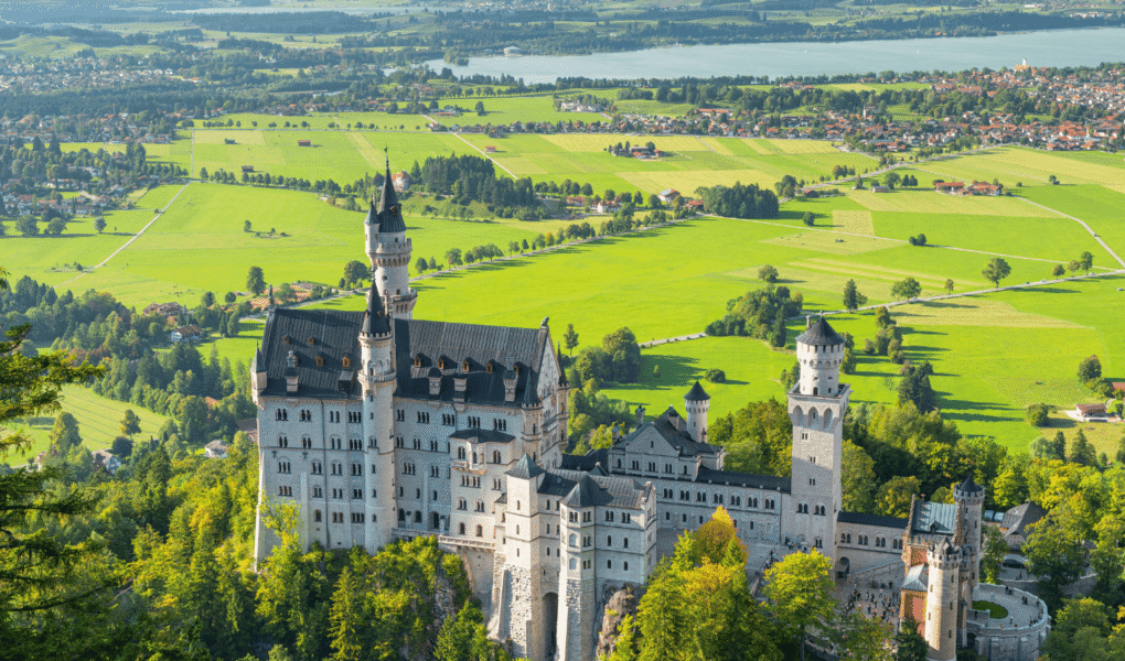 Aerial view of Neuschwanstein Castle perched above lush green fields and villages in southern Bavaria, Germany.
