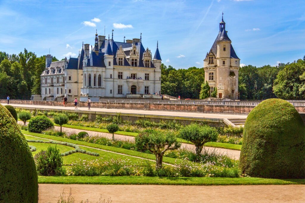 Château de Chenonceau with formal gardens and visitors crossing the bridge on a sunny summer day