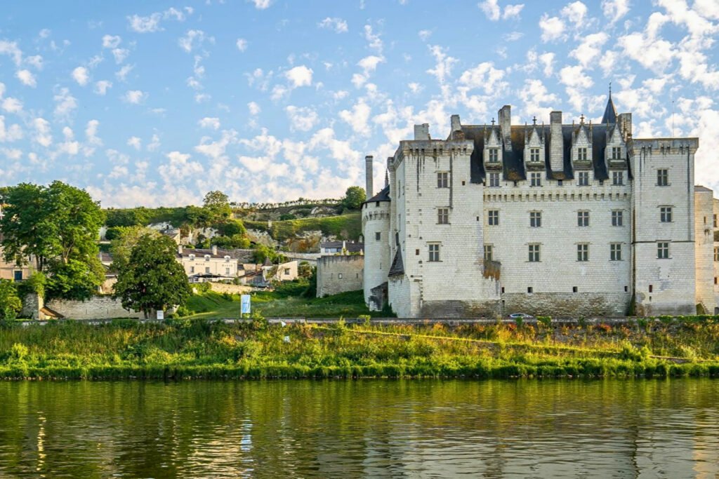 Château de Montsoreau along the Loire River under a blue sky, with its stone walls reflecting on the calm water