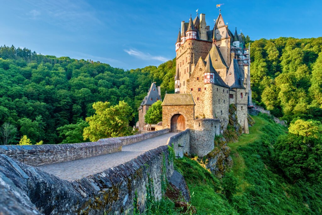 Eltz Castle entrance glowing in golden sunlight with lush green hills in the background