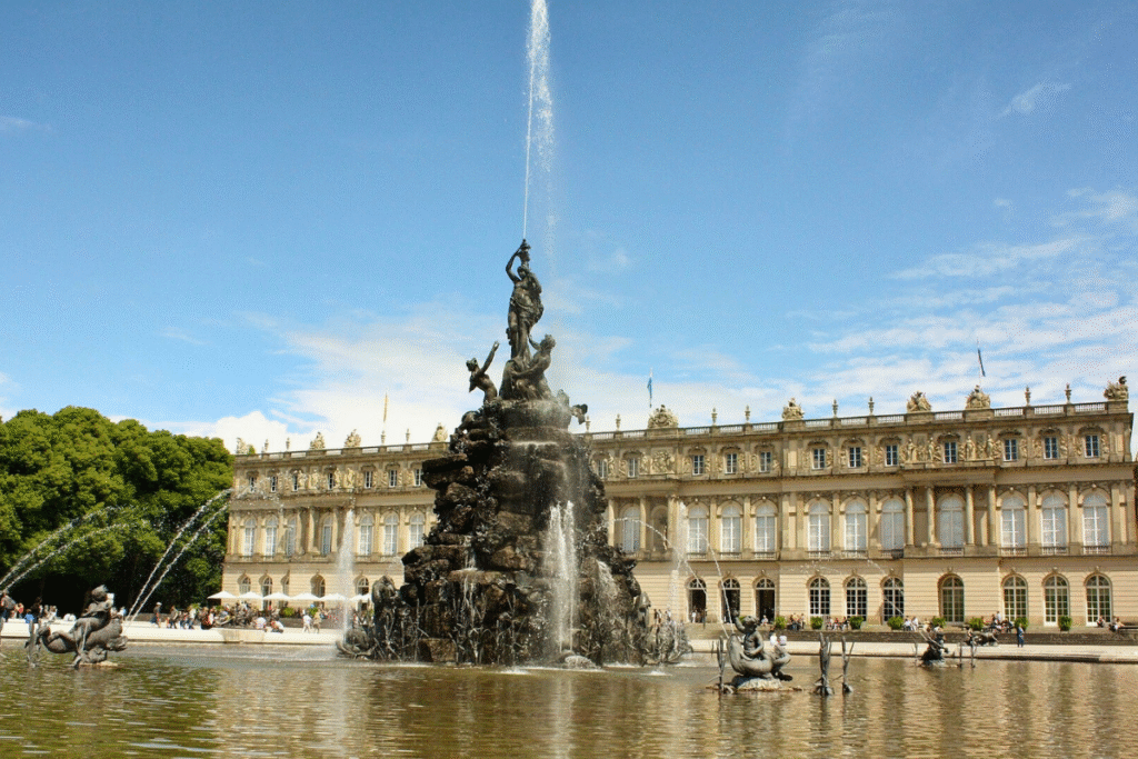 Wide view of Herrenchiemsee Palace with the grand Latona Fountain spraying water in the foreground, set on Herreninsel Island in Lake Chiemsee.