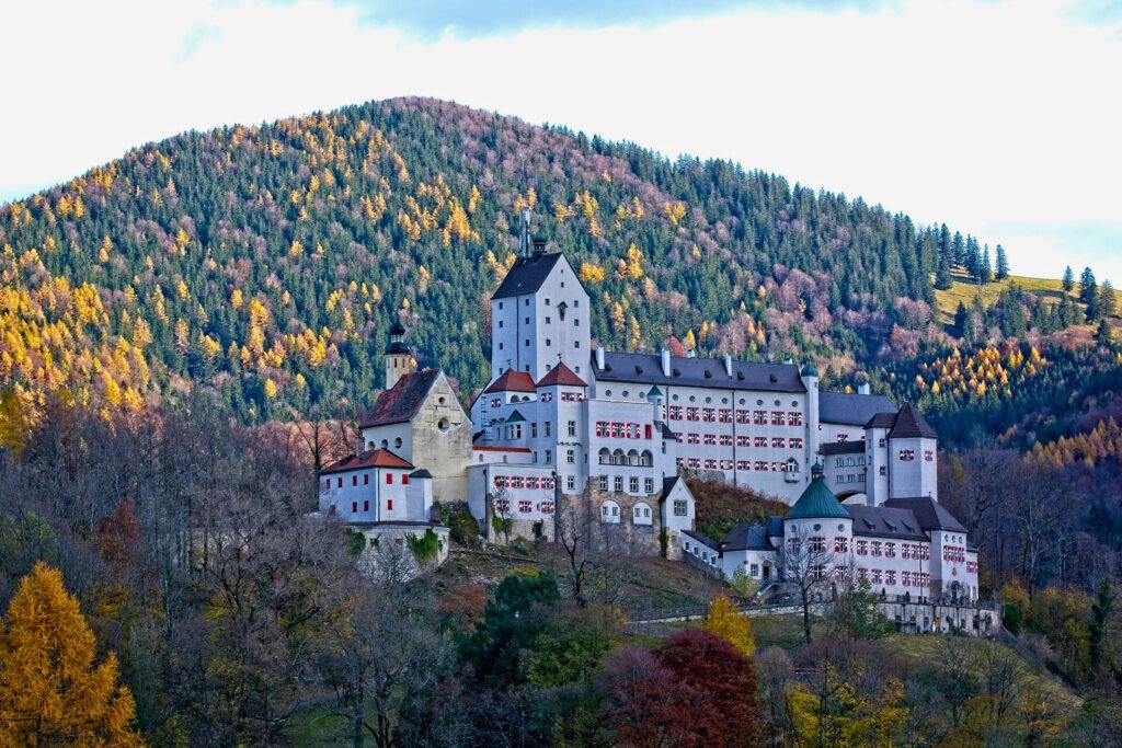 Aerial view of Hohenaschau Castle in Bavaria, surrounded by colorful autumn forest on a hillside.